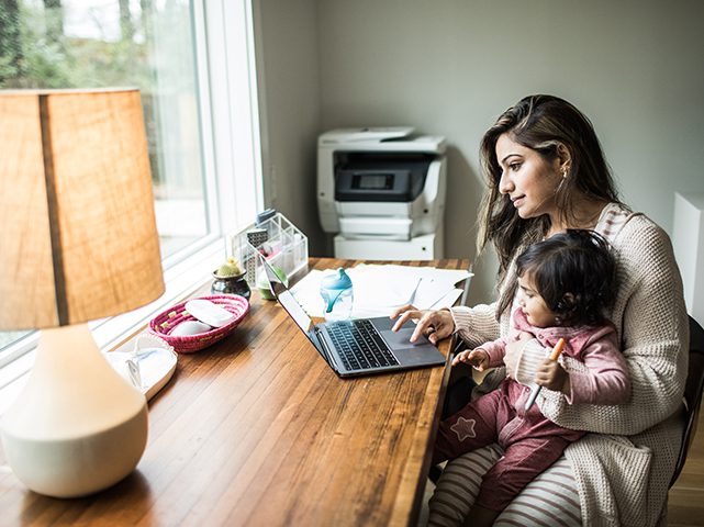 woman working at home on computer while holding child