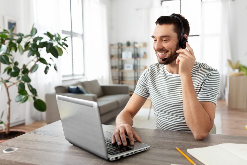 employee sitting at home workspace wearing a headset and engaging with clients on laptop