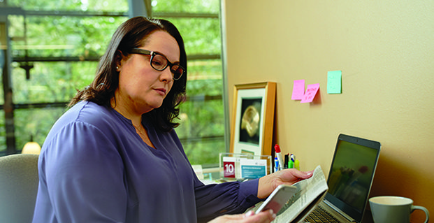 candidate sititng in front of workspace at home holding newspaper and phone