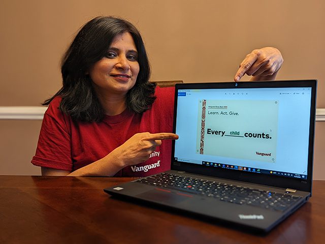 Vanguard crew member sitting at table pointing to laptop with powerpoint presentation on screen.