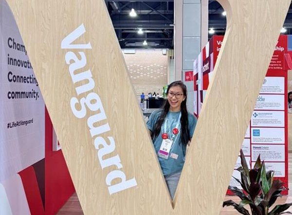 Justina posing in between a large wooden Vanguard “V” sign at the Grace Hopper event.