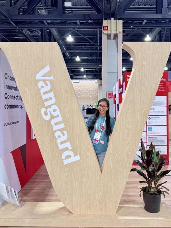 Justina posing in between a large wooden Vanguard “V” sign at the Grace Hopper event.